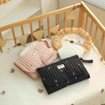 Tapis à langer nomade rose et noir, vue sur le produit dans une lit de bébé